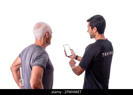 Ein Fitnesstrainer erklärt einem älteren Mann-Client, wie eine Software-Anwendung für das Training auf einem weißen isolierten Hintergrund verwendet wird. Stockfoto