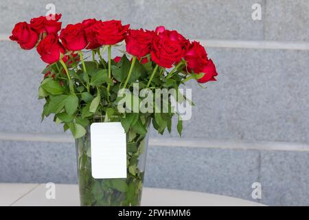 Blumenstrauß aus roten Rosen in einer Vase und eine weiße Note zum Schreiben eines Grußwortes. Stockfoto