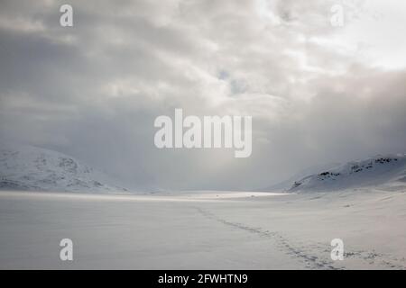 Schneeschuhwandern auf einem gefrorenen See, der sich bei Sonnenuntergang den Alesjaure Hütten nähert, Kungsleden Trail, Schwedisch Lappland, April 2021. Stockfoto