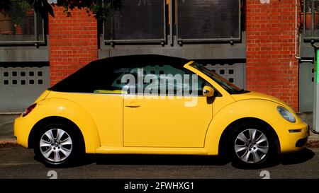 Leuchtend gelbe zweitürige Volkswagen Beetle vor geparkt Ein Backsteingebäude in Brisbane, Australien Stockfoto