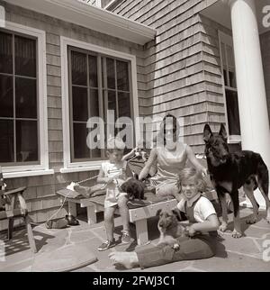 14. August 1963 Hyannis Port – Squaw Island - Präsident John F. Kennedy (telefonisch, mit Sonnenbrille), First Lady Jacqueline Kennedy und ihre Kinder Caroline Kennedy und John F. Kennedy, Jr., sitzen mit ihren Hunden Wolf, White Tips, Blackie und Clipper, Im Brambletyde-Haus auf Squaw Island, Hyannis Port, Massachusetts. Stockfoto