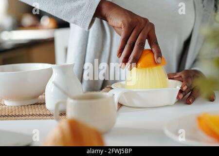 Hände einer Frau, die bei der Herstellung von frischem Orange einen manuellen Entsafter verwendet Getränk an der Küchentheke Stockfoto
