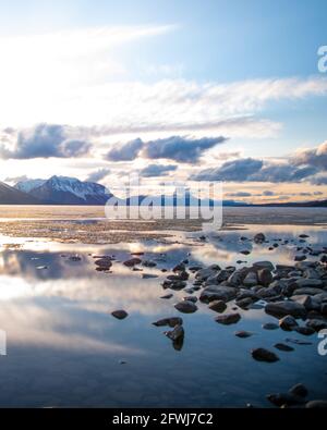 Malerische Landschaft im Norden Kanadas im Frühling mit Felsen, schneebedeckten Bergen in der Ferne in ruhigem Seewasser am bewölkten Nachmittag. Stockfoto