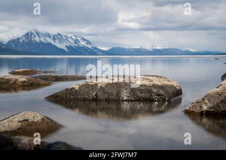 Malerische Landschaft im Norden Kanadas im Frühling mit Felsen, schneebedeckten Bergen Reflexion in ruhigen See Wasser am bewölkten Nachmittag. Stockfoto