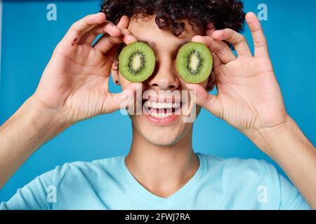 Mann mit lockigem Haar, der Kiwi in der Nähe des Klassengesichts hält Stockfoto