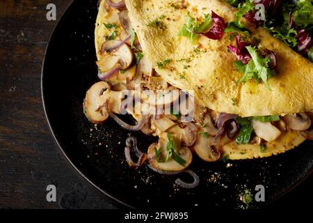 Von oben ein leckeres Omelett mit Pilzen und Zwiebeln garniert Mit frischem Salat auf dem Teller auf dem Tisch Stockfoto