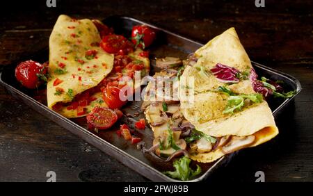 Hoher Winkel von leckeren Omelettes mit Pilzen und Tomaten auf Tablett auf dunklen Tisch gelegt Stockfoto