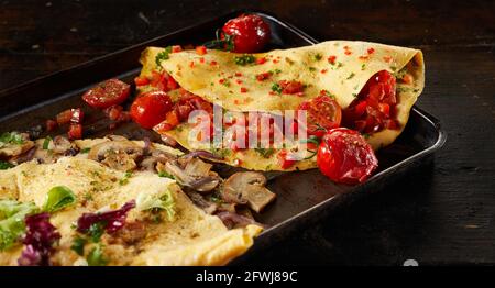 Von oben von leckeren Omelettes mit Pilzen und Tomaten auf Tablett serviert auf dem Tisch zum Mittagessen Stockfoto