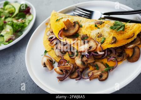 Hoher Winkel von leckeren Omelette mit Pilzen und Petersilie platziert Auf dem Tisch mit Salat zum Mittagessen Stockfoto