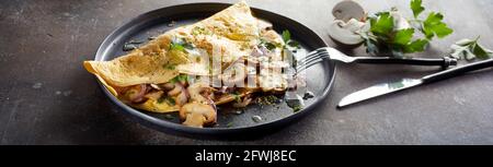 Hoher Panoramablick auf das köstliche Omelett mit Pilzen Und Petersilie in Teller auf dem Tisch mit Messer und serviert Gabel Stockfoto