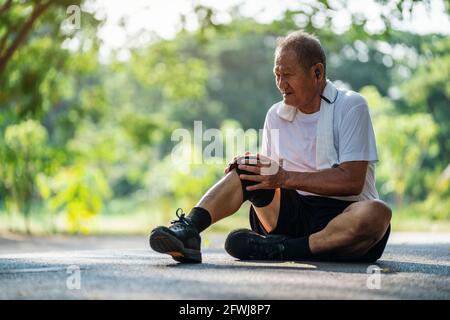 Asiatischer älterer Mann, der während des Trainings im Park unter Knieschmerzen leidet. Stockfoto