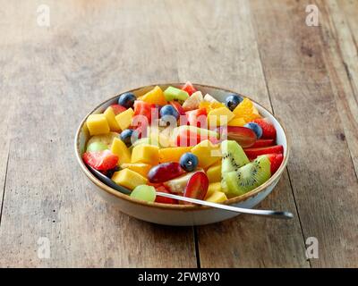 Schüssel mit buntem frischem Obstsalat auf Holzküchentisch Stockfoto