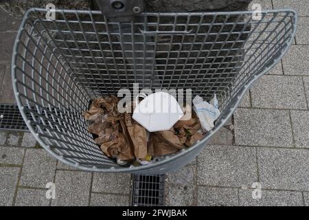 Gesichtsmaske im öffentlichen Abfalleimer. Gebrauchte Maske, die in einem Staubbehälter aus Metalldraht im Freien entsorgen wird. High-Angle-Ansicht. Stockfoto