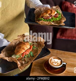 Konzept für Essen, Frühstück, Morgen und Mittagessen. Frisches Croissant-Sandwich mit Schinken, Käse in den Händen eines Kellners. Foto für das Menü. Stockfoto