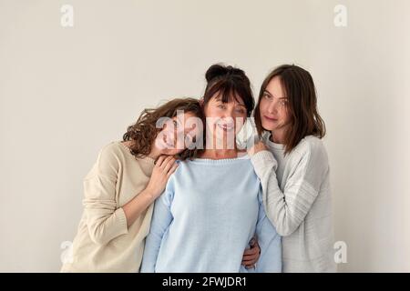 Fröhliche Erwachsene Mutter umarmt charmante junge Töchter im Stehen Weißer Hintergrund im Studio und Blick auf die Kamera Stockfoto