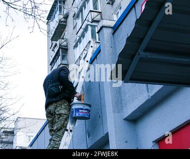 Dnepropetrovsk, Ukraine - 03.29.2021: Das Werk des Malers steht an der Spitze. Ein Mitarbeiter malt die Fassade eines Gebäudes, während er auf der Treppe steht. Stockfoto