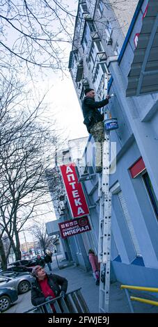 Dnepropetrovsk, Ukraine - 03.29.2021: Das Werk des Malers steht an der Spitze. Ein Mitarbeiter malt die Fassade eines Gebäudes, während er auf der Treppe steht. Stockfoto