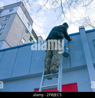 Dnepropetrovsk, Ukraine - 03.29.2021: Das Werk des Malers steht an der Spitze. Ein Mitarbeiter malt die Fassade eines Gebäudes, während er auf der Treppe steht. Stockfoto