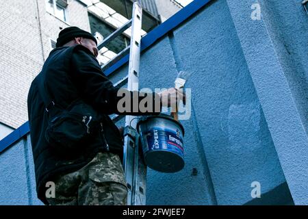 Dnepropetrovsk, Ukraine - 03.29.2021: Das Werk des Malers steht an der Spitze. Ein Mitarbeiter malt die Fassade eines Gebäudes, während er auf der Treppe steht. Stockfoto