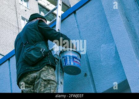 Dnepropetrovsk, Ukraine - 03.29.2021: Das Werk des Malers steht an der Spitze. Ein Mitarbeiter malt die Fassade eines Gebäudes, während er auf der Treppe steht. Stockfoto