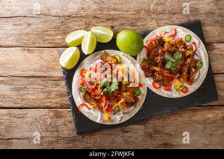 Heiße Tacos mit gegrilltem Schweinebauch, Gemüse der Saison, Cheddar und Limette aus nächster Nähe auf einem Schieferbrett auf dem Tisch. Horizontale Draufsicht von oben Stockfoto