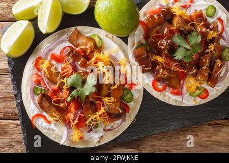 Würzige Tacos mit gegrilltem Schweinebauch, Gemüsesalsa, Käse aus nächster Nähe auf einem Schiefertafel auf dem Tisch. Horizontale Draufsicht von oben Stockfoto