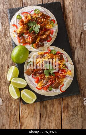 Frisch zubereitete Tacos mit gegrilltem Schweinebauch, Käse und frischem Gemüse aus der Nähe auf einem Schiefertafel auf dem Tisch. Vertikale Draufsicht von oben Stockfoto