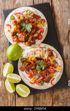 Mesican Tacos mit Gemüse, gegrilltem Schweinebauch, Käse und Limette aus nächster Nähe auf einem Schiefertafel auf dem Tisch. Vertikale Draufsicht von oben Stockfoto