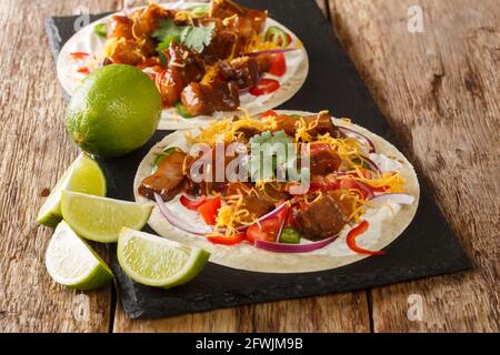 Heiße Tacos mit gegrilltem Schweinebauch, Gemüse der Saison, Cheddar und Limette aus nächster Nähe auf einem Schieferbrett auf dem Tisch. Horizontal Stockfoto