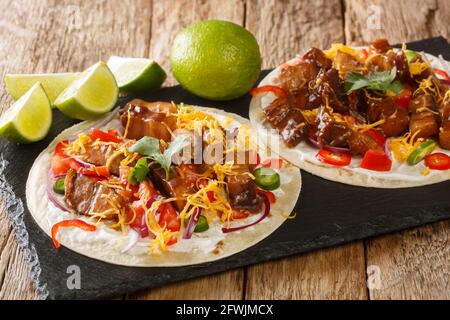 Köstliche hausgemachte Tacos mit gegrilltem Schweinebauch, Gemüsesalsa, Cheddar und Limette aus nächster Nähe auf einem Schieferbrett auf dem Tisch. Horizontal Stockfoto