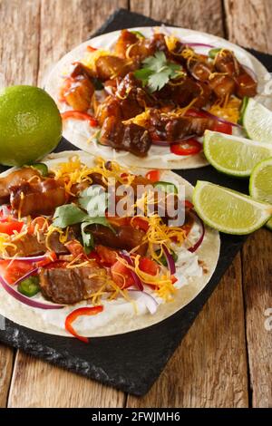 Frisch zubereitete Tacos mit gegrilltem Schweinebauch, Käse und frischem Gemüse aus der Nähe auf einem Schieferbrett auf dem Tisch. Vertikal Stockfoto