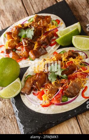 Mesican Tacos mit Gemüse, gegrilltem Schweinebauch, Käse und Limette in der Nähe auf einem Schiefertafel auf dem Tisch. Vertikal Stockfoto