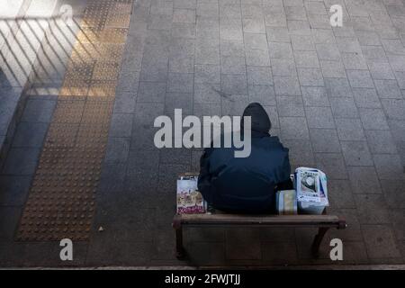 Ein obdachloser Mann liest, während er auf einer Bank in einem kleinen Park in Tokio ruht. Stockfoto