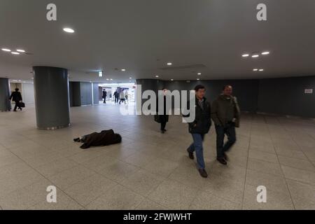 Marunouchi, Tokio, Japan. Januar 2015. Salarymen oder Büroangestellte gehen an einem japanischen Obdachlosen vorbei, der in den Einkaufspassagen unter dem Bahnhof Tokio auf dem Boden schläft. Quelle: Damon Coulter/SOPA Images/ZUMA Wire/Alamy Live News Stockfoto