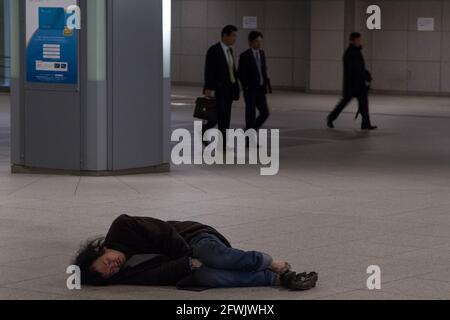 Marunouchi, Tokio, Japan. Januar 2015. Salarymen oder Büroangestellte gehen an einem japanischen Obdachlosen vorbei, der in den Einkaufspassagen unter dem Bahnhof Tokio auf dem Boden schläft. Quelle: Damon Coulter/SOPA Images/ZUMA Wire/Alamy Live News Stockfoto