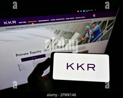 Person, die ein Mobiltelefon mit dem Unternehmenslogo der US-Investmentfirma KKR and Co. Inc. Auf dem Bildschirm vor der Unternehmenswebsite hält. Konzentrieren Sie sich auf die Telefonanzeige. Stockfoto