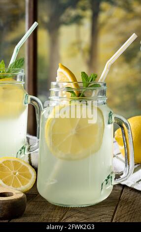 Nahaufnahme der Limonade in einem Glas mit Zitrone Scheiben durch ein Fenster mit einer ländlichen Hintergrundszene Stockfoto