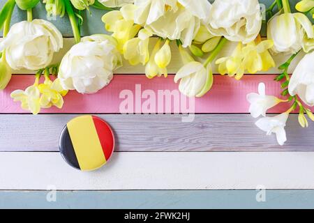 Belgien Flagge auf Knopf Abzeichen und schöne Blumen auf gestreiftem Holzhintergrund gedruckt, Kopierraum. Stockfoto