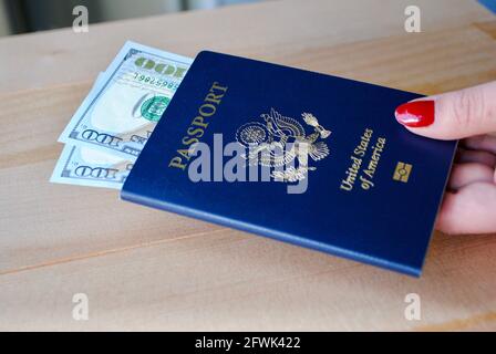 Weibliche Finger mit amerikanischem Pass und Dollarscheinen auf Holzhintergrund. Reisekonzept. Stockfoto