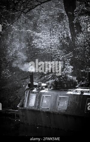 Ein launiges Schwarz-Weiß-Bild eines Barges, der auf dem Leeds & Liverpool-Kanal festgemacht ist, mit Rauch, der aus seinem Kamin an der Apperley Bridge, Yorkshire, steigt Stockfoto