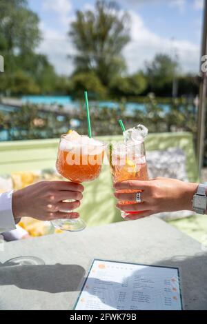 Zwei Personen jubeln mit Cocktails draußen auf einer sonnigen Terrasse und einem blauen Pool im Hintergrund Stockfoto