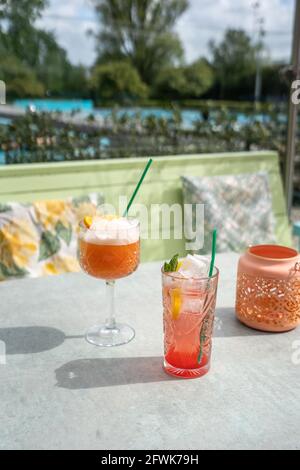 Pinke Cocktails, die draußen auf einer sonnigen Terrasse mit einem serviert werden Grüne Couch und ein blauer Swimmingpool im Hintergrund Stockfoto