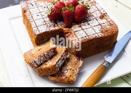 Quadratischer Kuchen mit Scheiben und Messer auf weißem Teller mit Erdbeeren darauf Stockfoto