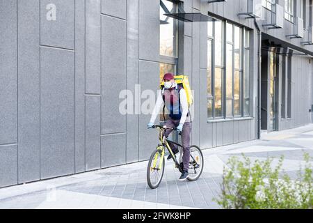 Ein junger Kurier liefert Essen mit einem gelben Thermalrucksack und fährt mit dem Fahrrad in der Stadt. Konzept für den Lieferservice von Lebensmitteln Stockfoto