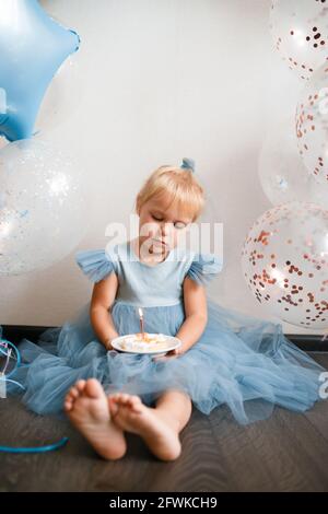 Das kleine blonde Mädchen bläst die Kerzen auf dem Geburtstagskuchen aus. Stockfoto
