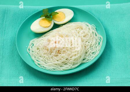 Ideyappam oder Noolappam, südindisches Frühstück, das wunderschön arrangiert ist Mit zwei Scheiben gekochter Eier in aquamarinfarbener Farbe Tafelgeschirr pla Stockfoto