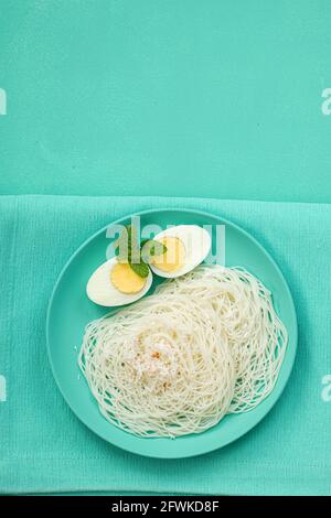 Ideyappam oder Noolappam, südindisches Frühstück, das wunderschön arrangiert ist Mit zwei Scheiben gekochter Eier in aquamarinfarbener Farbe Tafelgeschirr pla Stockfoto