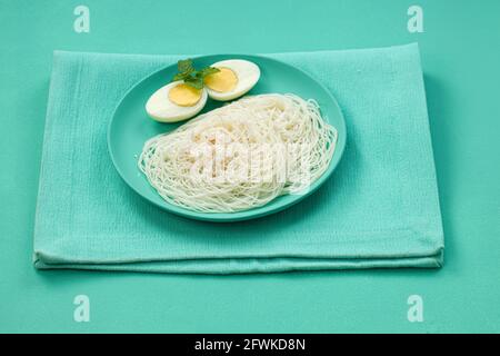 Ideyappam oder Noolappam, südindisches Frühstück, das wunderschön arrangiert ist Mit zwei Scheiben gekochter Eier in aquamarinfarbener Farbe Tafelgeschirr pla Stockfoto