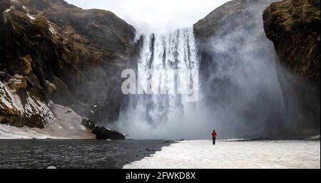 Skogafoss Wasserfall mit einsamer Person, die in der Nähe des Flusses steht. Winterszene im Süden Islands. Stockfoto