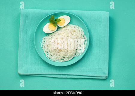 Ideyappam oder Noolappam, südindisches Frühstück, das wunderschön arrangiert ist Mit zwei Scheiben gekochter Eier in aquamarinfarbener Farbe Tafelgeschirr pla Stockfoto